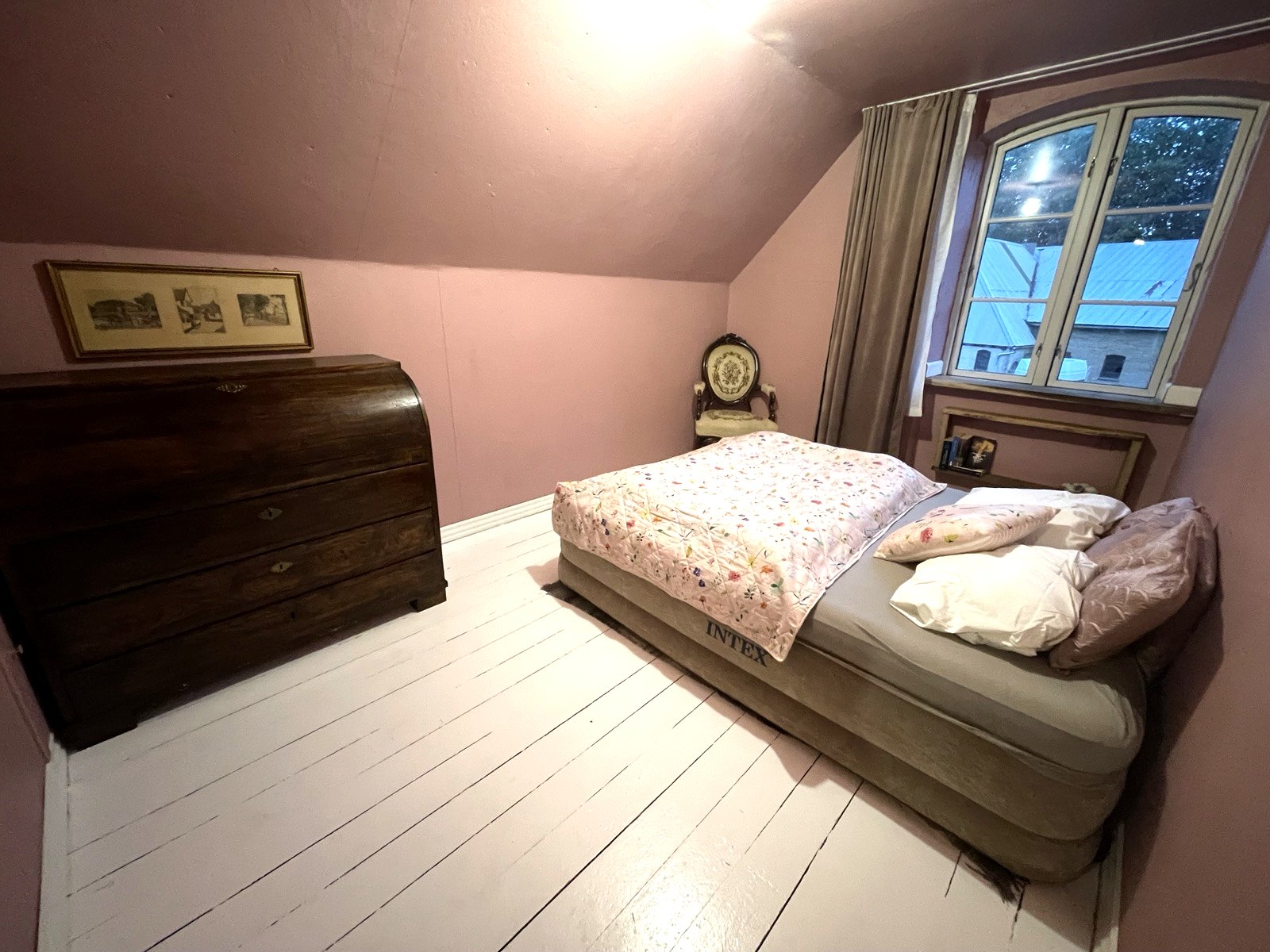 Zweites Doppelzimmer unter dem Dach mit rosa Wänden, weißem Dielenboden und alter Kommode